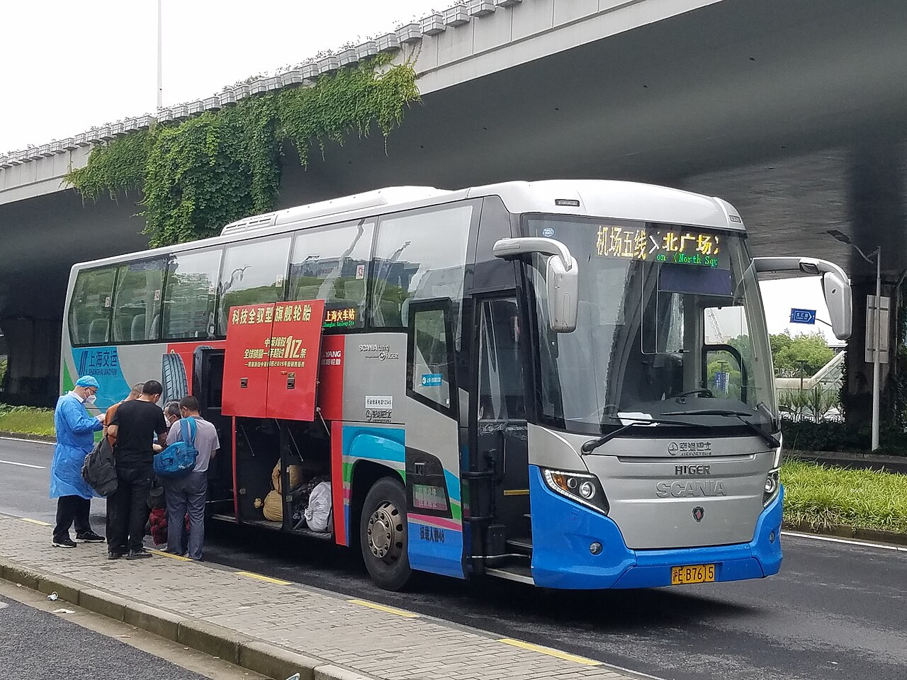 A blue and silver Higer-bodied Scania Touring coach boarding passengers.