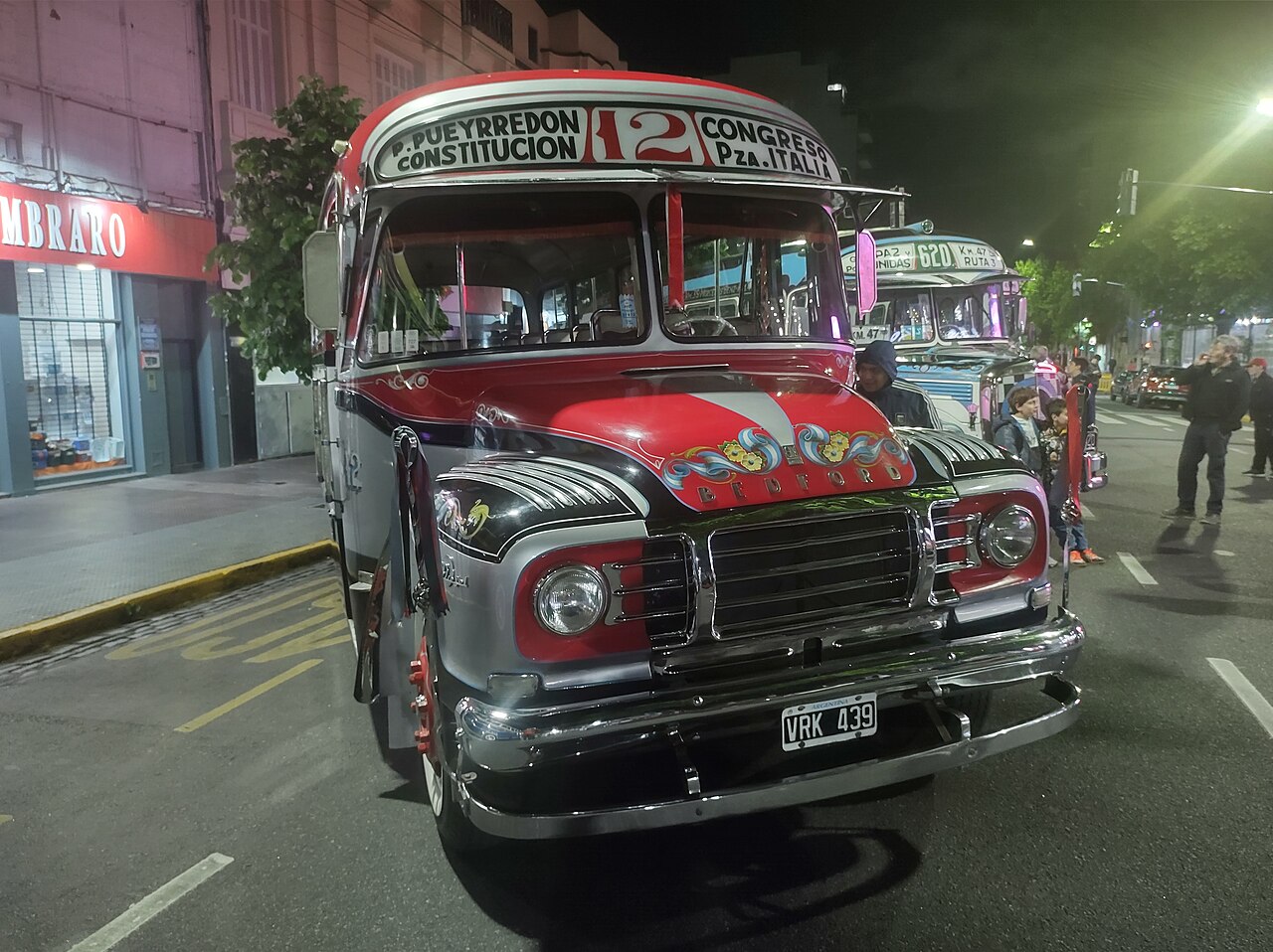 A restored classic Bedford colectivo of line 12 with full fileteado decoration, displayed at night.