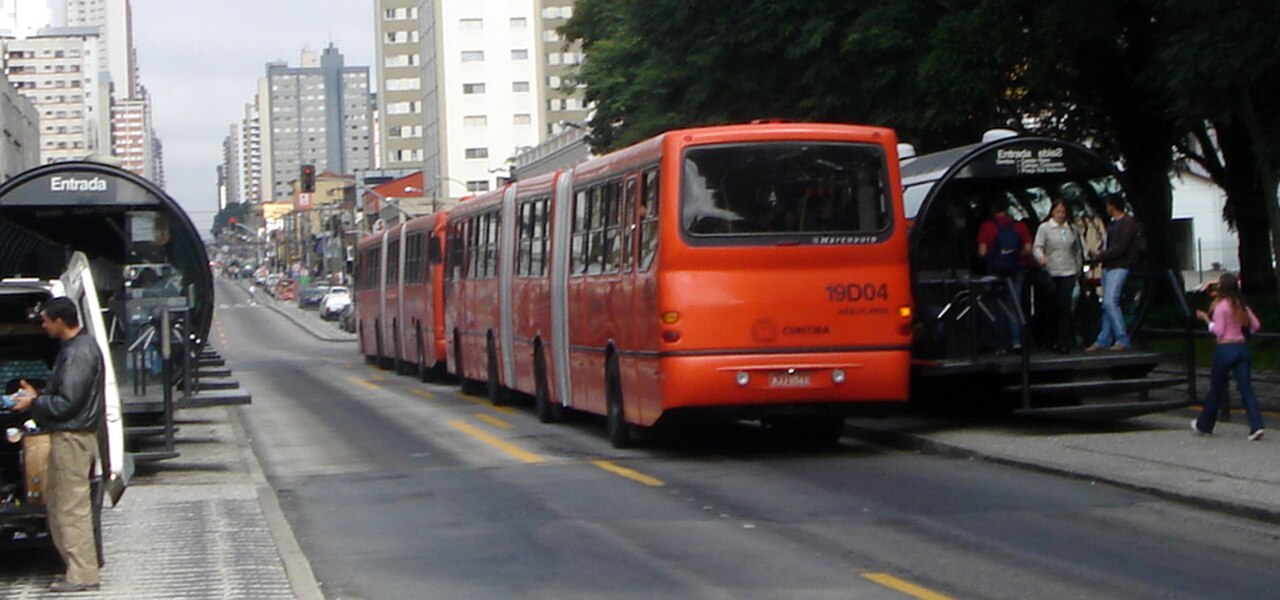 A bi-articulated bus on a dedicated Curitiba BRT corridor beside a tube station