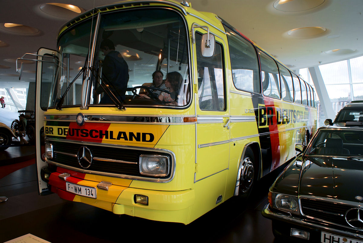 The preserved Mercedes-Benz O302 team bus of West Germany on display at the Mercedes-Benz Museum, painted yellow with a black-red-gold diagonal and "BR Deutschland" lettering.