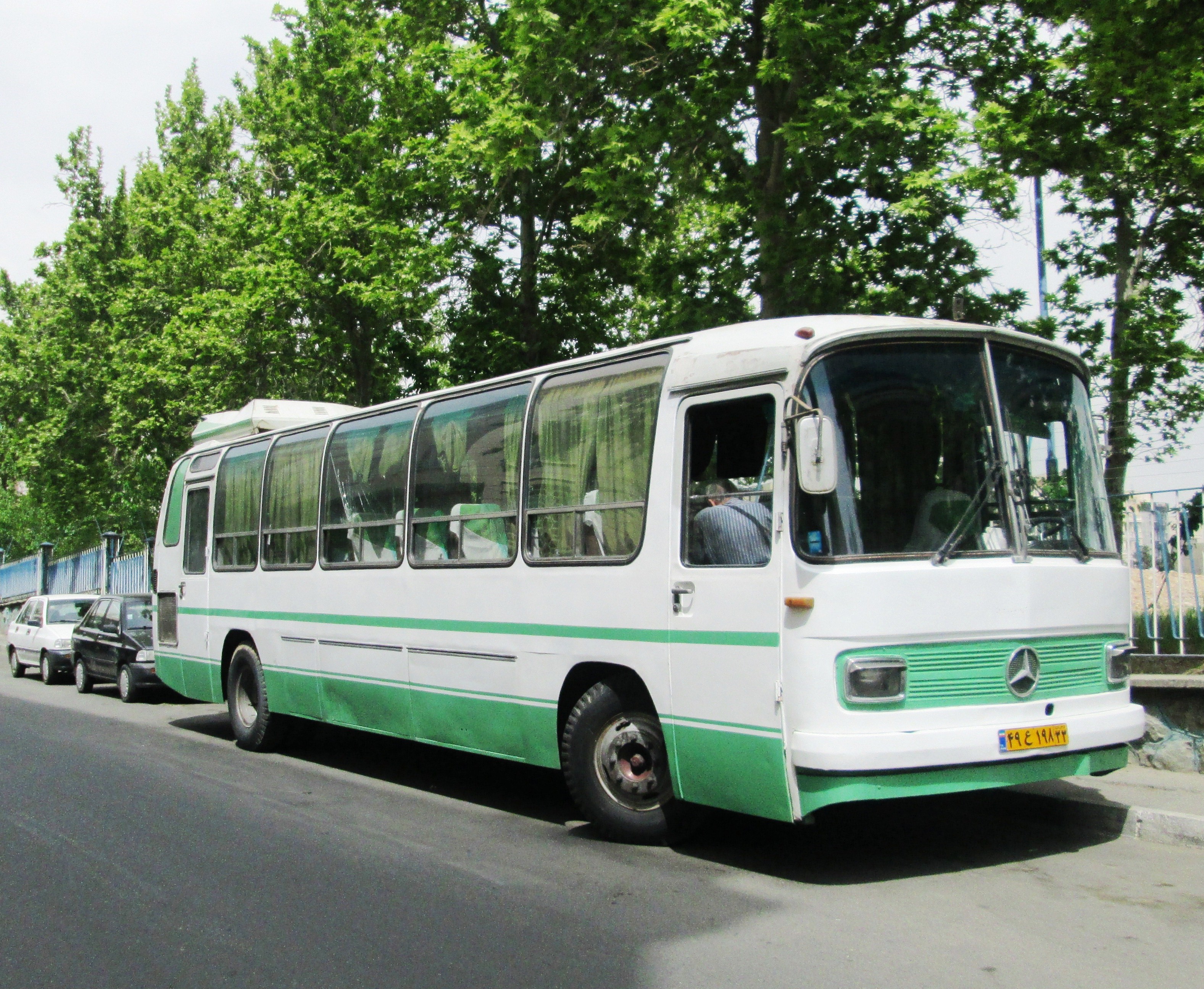 A white and green Mercedes-Benz O302, built locally by Iran Khodro Diesel, parked on a street in Tehran.