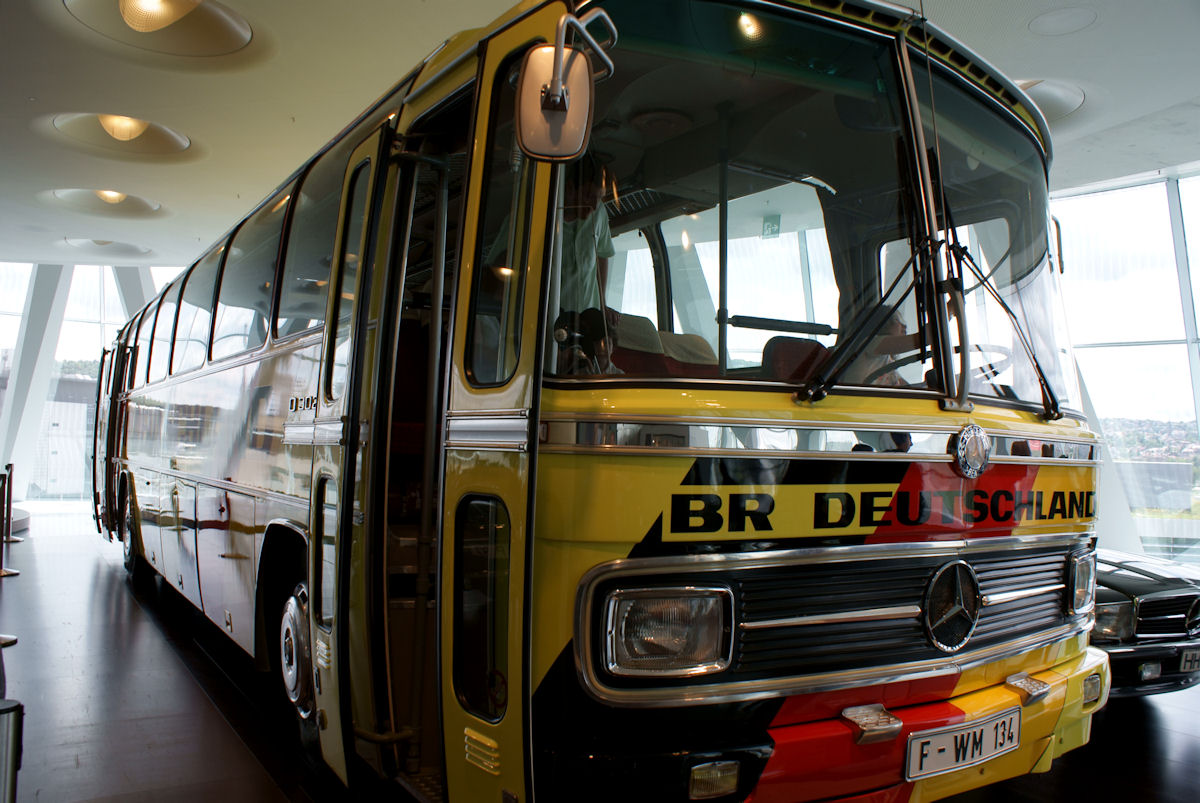 Front three-quarter view of the yellow West Germany O302 team bus with 'BR Deutschland' lettering and the O 302 badge on its side.