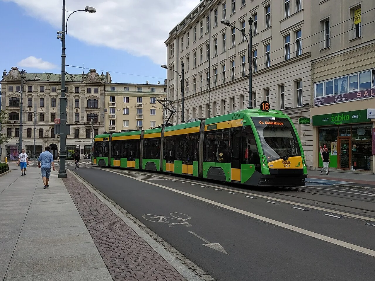 A green Solaris Tramino tram on a street in Poznań, Poland.