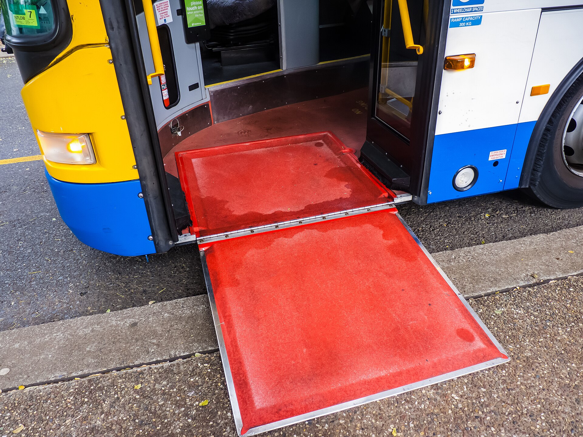 A low-floor city bus at a stop with its wheelchair boarding ramp folded out to the kerb for step-free access.