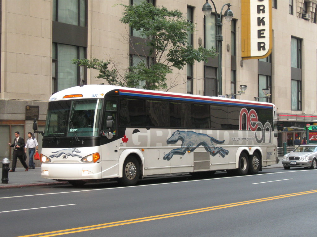 A blue-and-grey Greyhound MCI D4505 intercity coach picking up passengers on a New York City street.