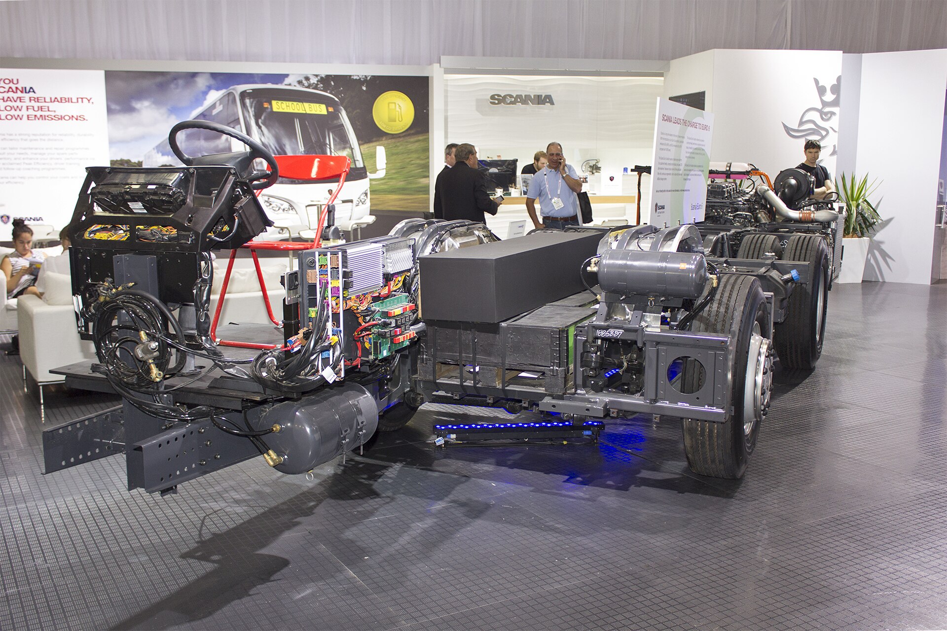 A bare Scania K320 bus chassis on display, with the longitudinal engine mounted behind the rearmost axle and no body fitted yet.