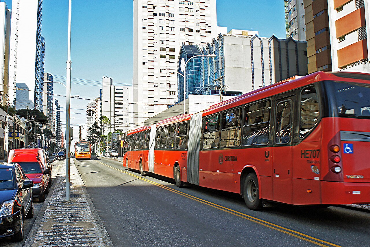 A long bi-articulated BRT bus on a dedicated busway in Curitiba, Brazil, its three sections stretched out along the exclusive lane.