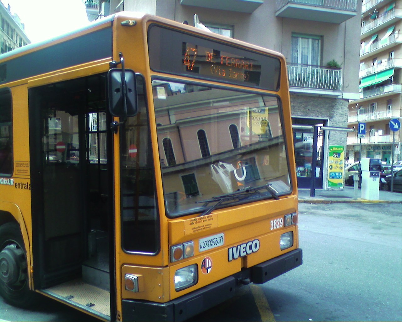 An orange Iveco TurboCity city bus with doors open at a stop in Genoa, Italy.
